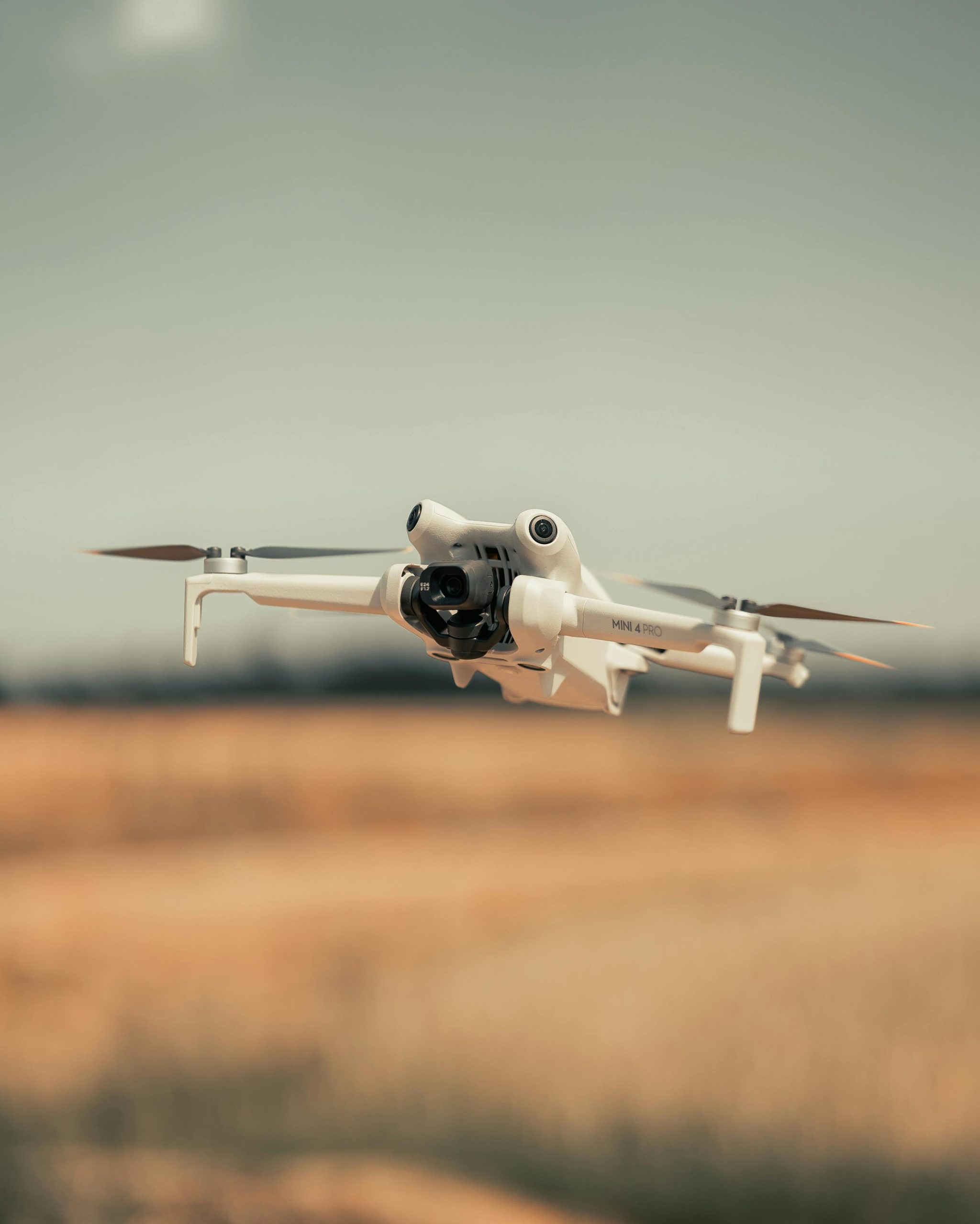 pexels-photo-31696718-31696718 White drone flying over a golden field on a clear day, showcasing modern technology.